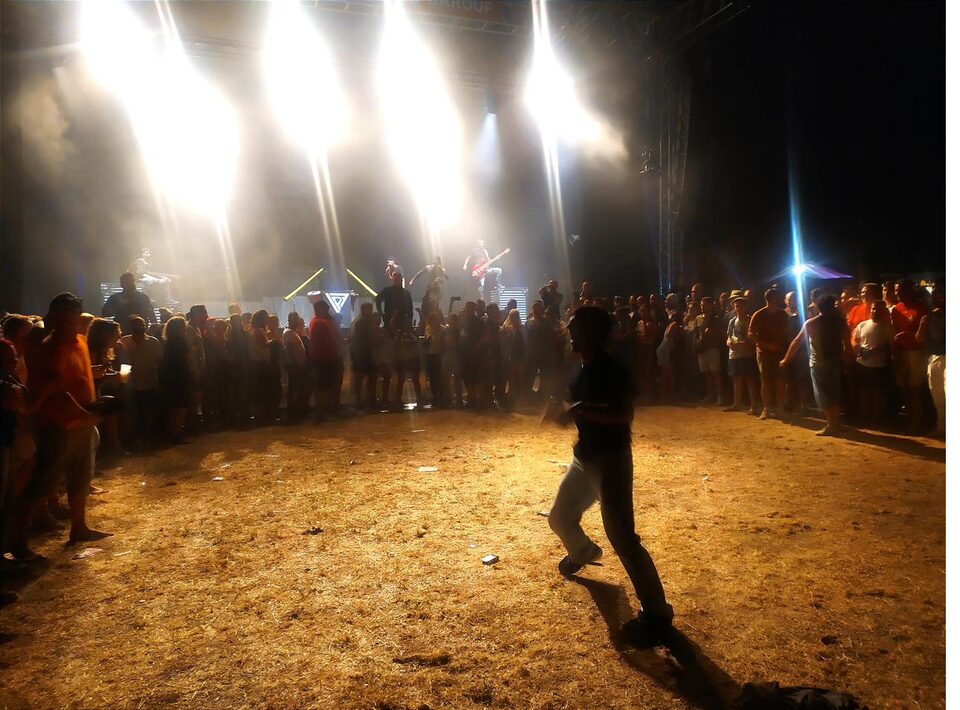 Concert de nuit en plein air, public debout face à une scène éclairée de jaune